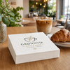 Hvite lunsjservietter 33x33 cm med logo plassert på et lyst trebord ved siden av en tallerken med en croissant