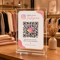 Eksklusivt gjennomsiktig akrylskilt med QR-kode for Instagram stående på en trebenk i en klesbutikk.